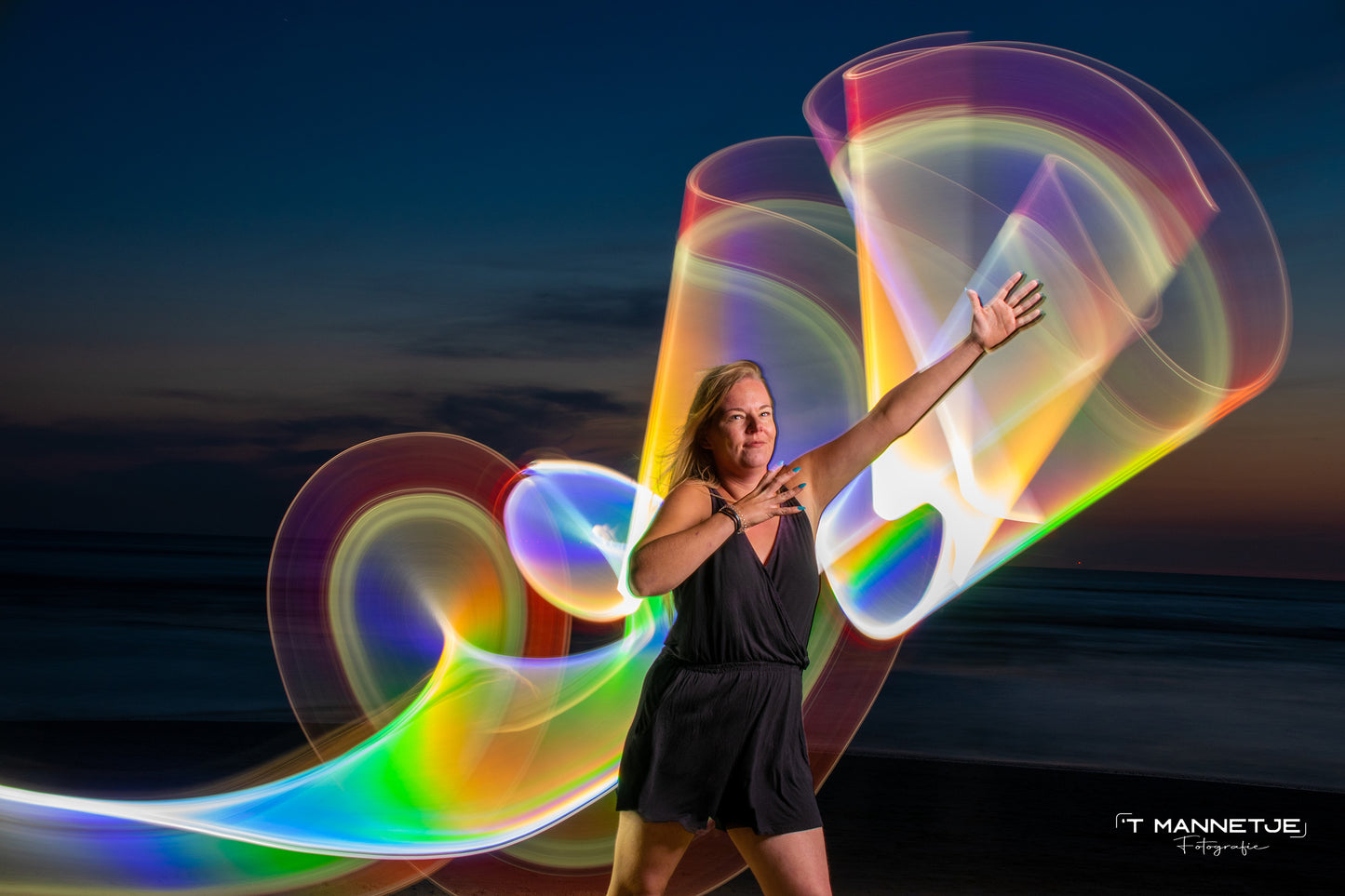Woman as model for light painting photography on the beach with rainbow silver holographic tube